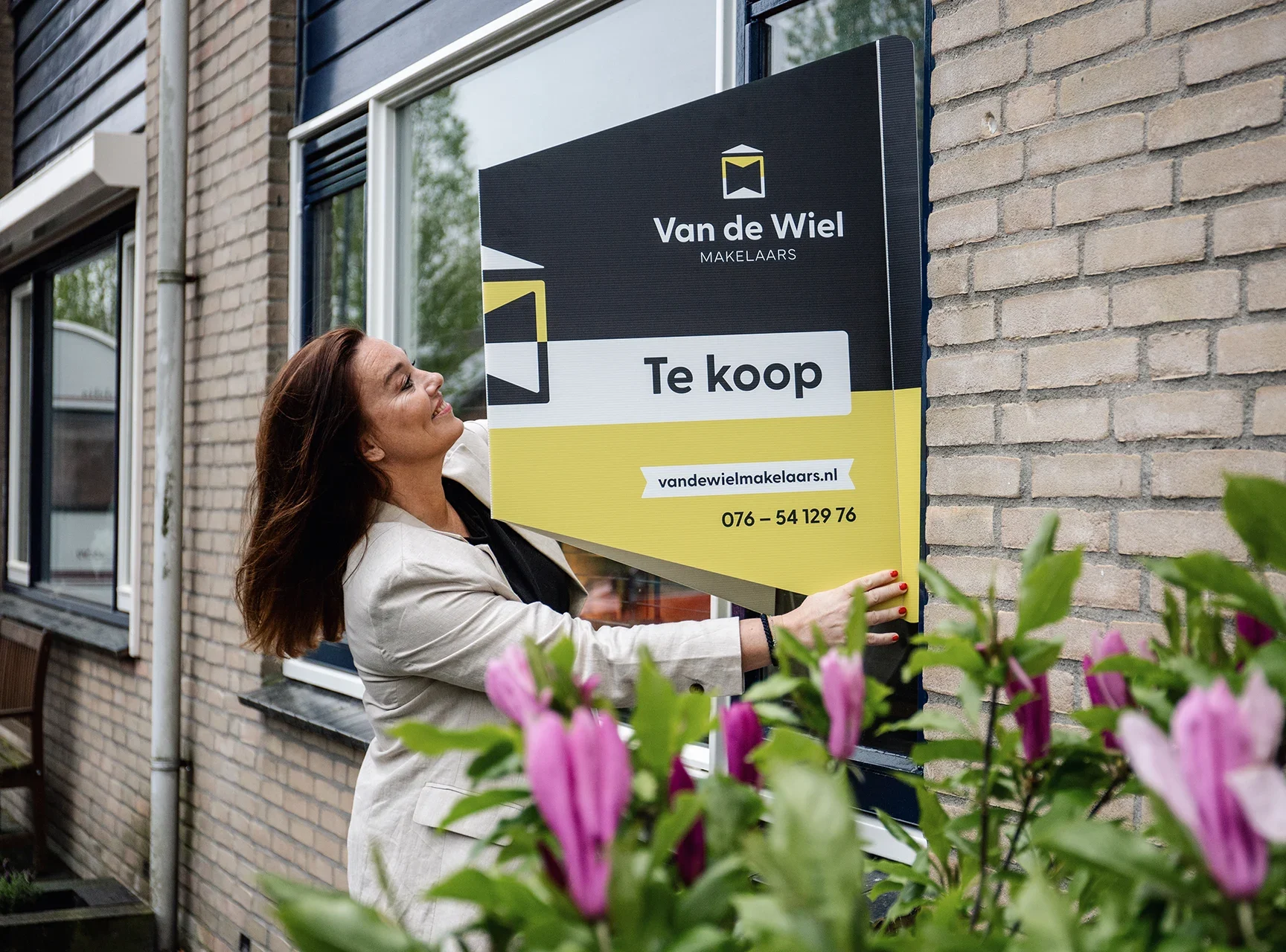 Karlijne plakt een te koop bord op de gevel van een woning in Breda