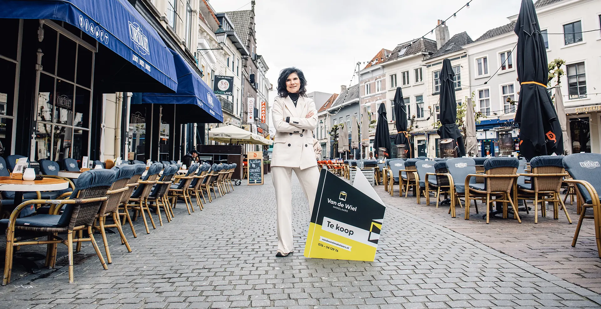 Mona staat bij het te koop bord van Van de Wiel in Breda bij gezellige terrassen